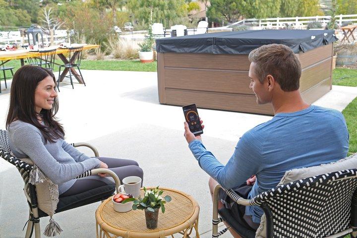 a man is sitting in front of woman, uses smartphone to control hot tub with smarttub application